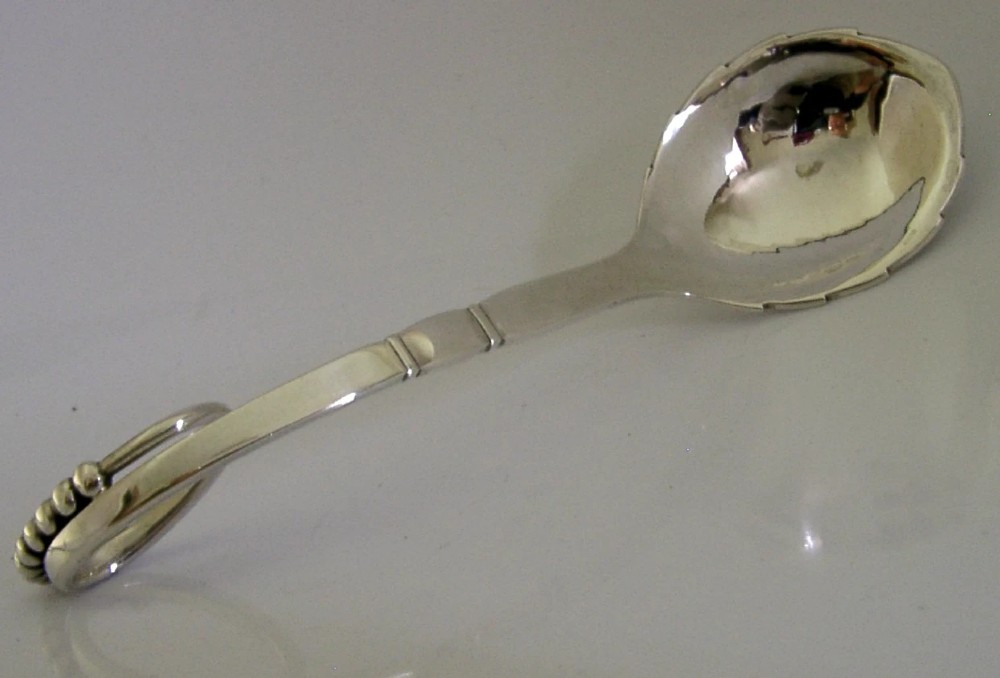 A sterling silver Georg Jensen spoon featuring a curved loop handle detailed with beaded ornamentation and a shallow oval bowl. View II