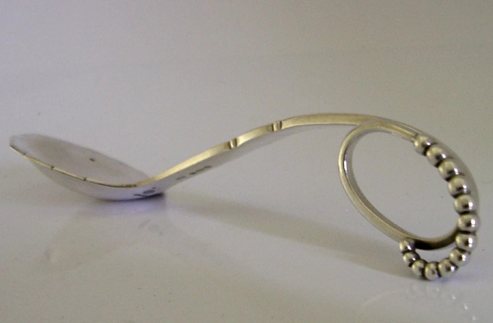 A sterling silver Georg Jensen spoon featuring a curved loop handle detailed with beaded ornamentation and a shallow oval bowl. View III