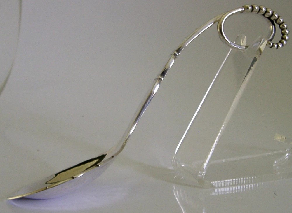 A sterling silver Georg Jensen spoon featuring a curved loop handle detailed with beaded ornamentation and a shallow oval bowl. View VII