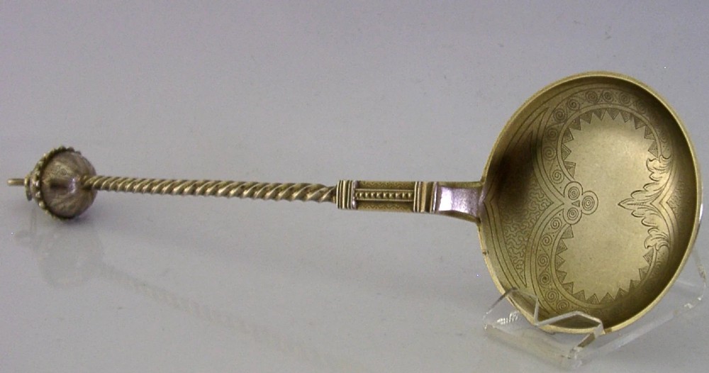 An antique Danish solid silver gilt serving spoon featuring an engraved circular bowl, a twisted stem, and a decorative finial.