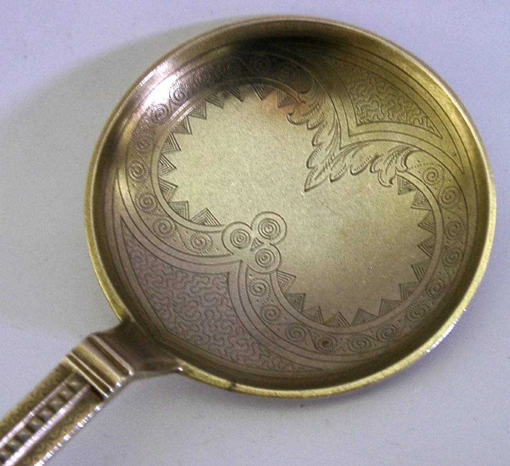 An antique Danish solid silver gilt serving spoon featuring an engraved circular bowl, a twisted stem, and a decorative finial. View II