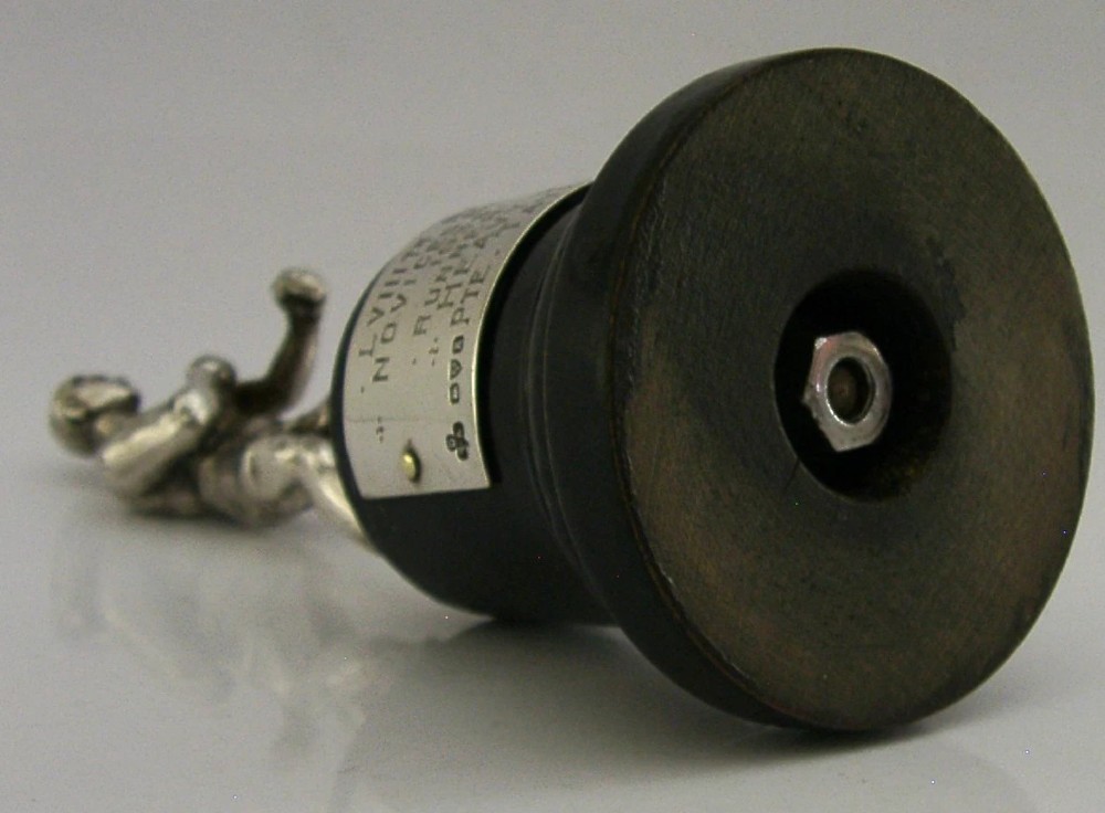 A silver-plated figurine of a boxer in a fighting stance mounted on a dark cylindrical wooden base with an engraved inscription plate. View V