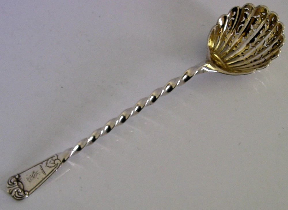 Victorian sterling silver sugar sifter spoon featuring a twisted stem, shell-shaped pierced bowl, and engraved heron crest handle terminal.