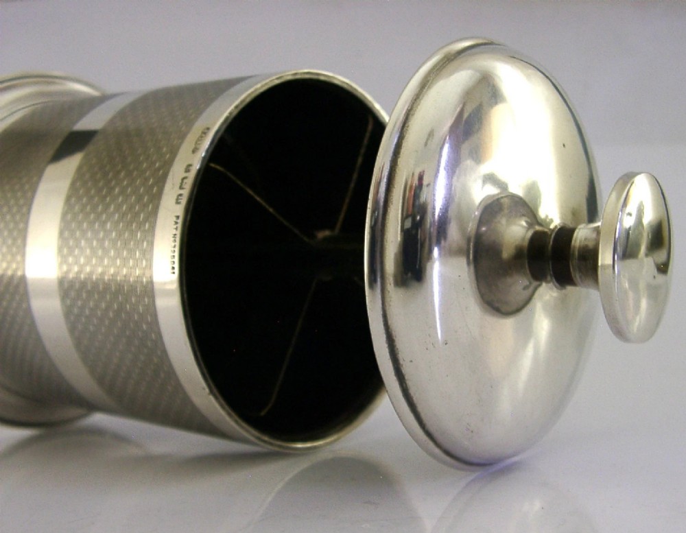 A cylindrical Art Deco sterling silver cigarette dispenser featuring engine-turned patterning, a central polished silver band, and a round knob finial on top. View IV