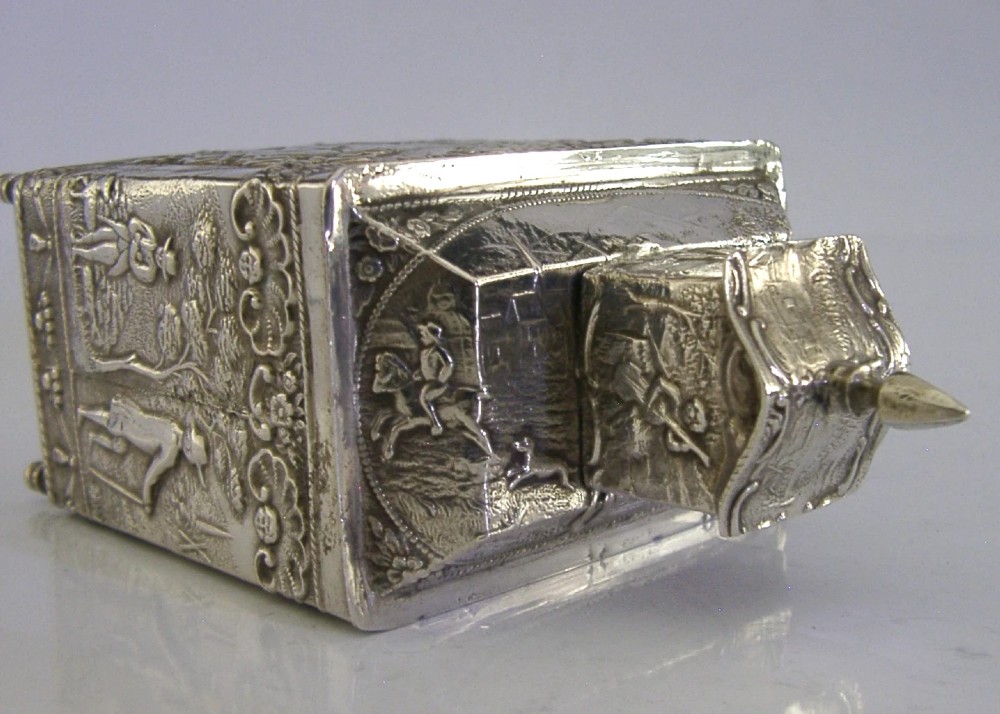 A rectangular solid silver tea caddy featuring relief-embossed pastoral scenes, turned feet, and a finial lid. View VI