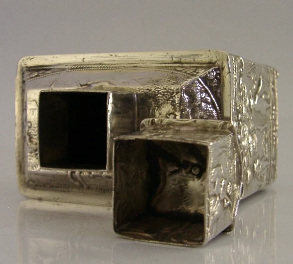 A rectangular solid silver tea caddy featuring relief-embossed pastoral scenes, turned feet, and a finial lid. View VIII