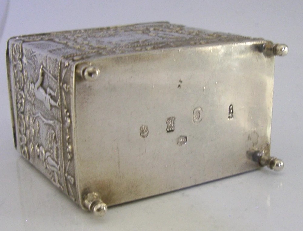 A rectangular solid silver tea caddy featuring relief-embossed pastoral scenes, turned feet, and a finial lid. View IX