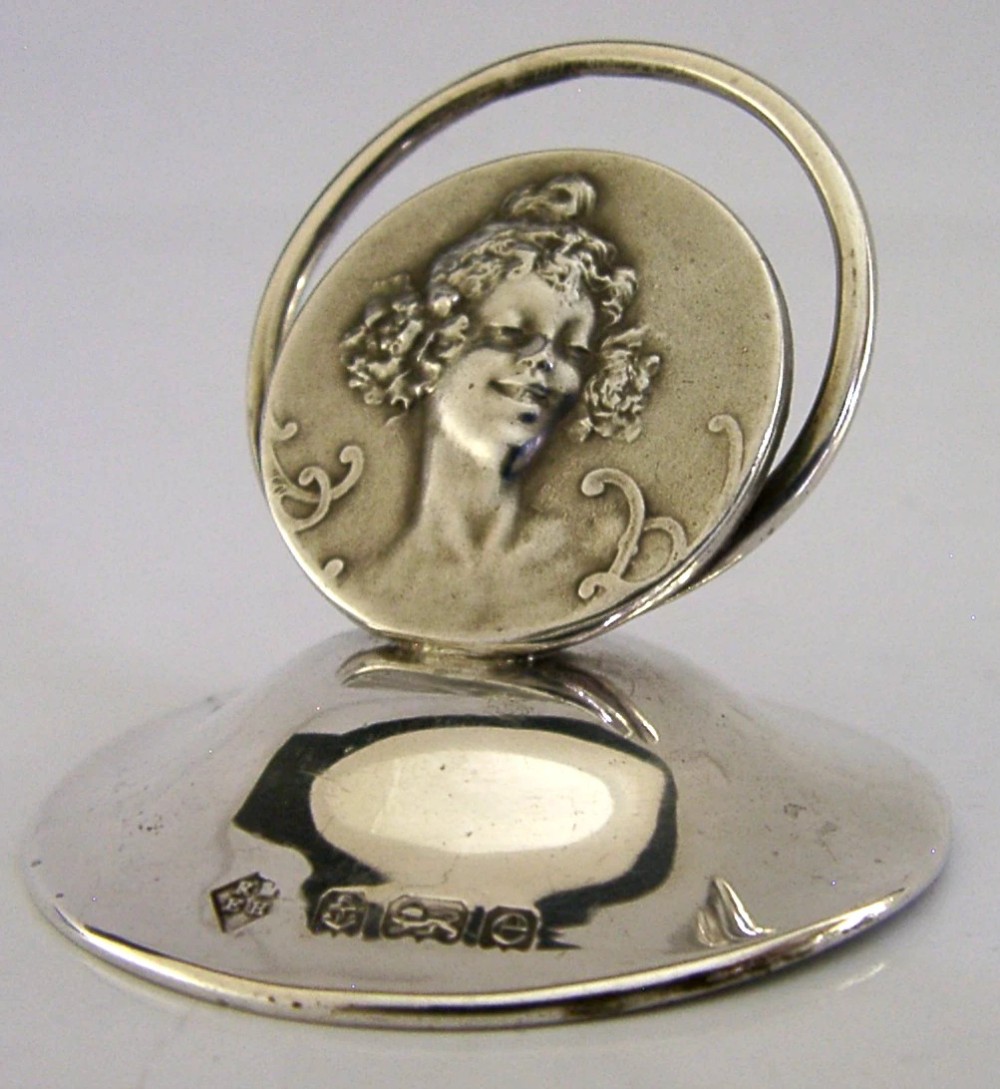 An Edwardian sterling silver menu holder featuring a circular relief of a maidens head set within an oval ring atop a domed base bearing British hallmarks.