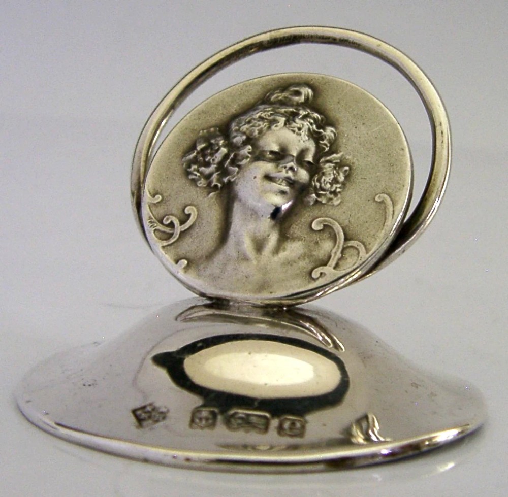 An Edwardian sterling silver menu holder featuring a circular relief of a maidens head set within an oval ring atop a domed base bearing British hallmarks. View IV