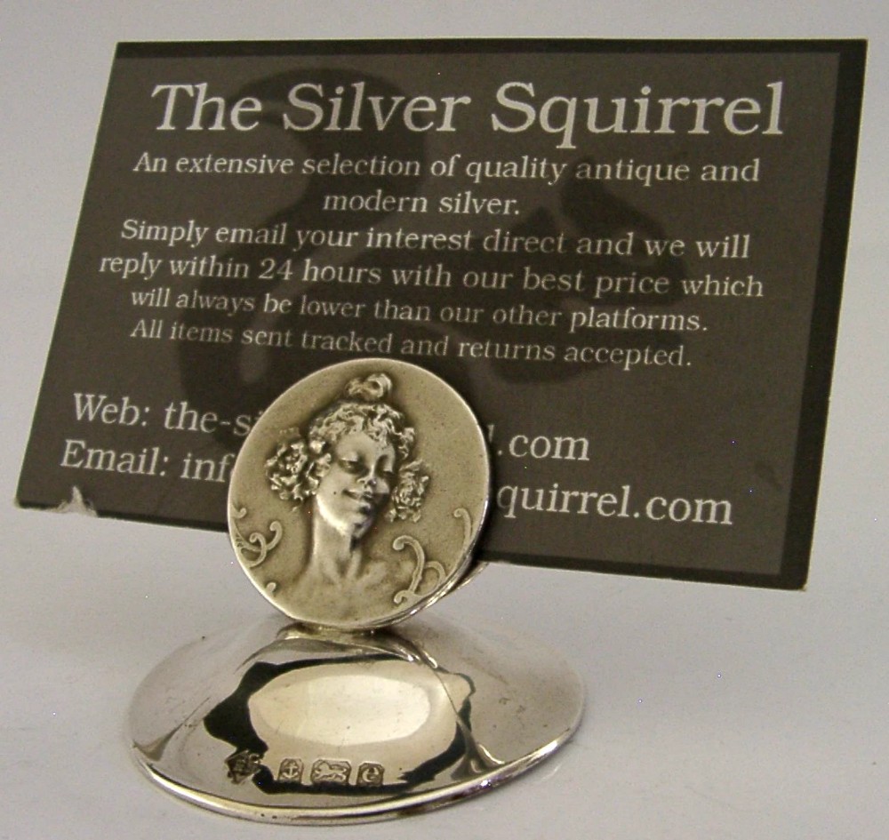 An Edwardian sterling silver menu holder featuring a circular relief of a maidens head set within an oval ring atop a domed base bearing British hallmarks. View VII