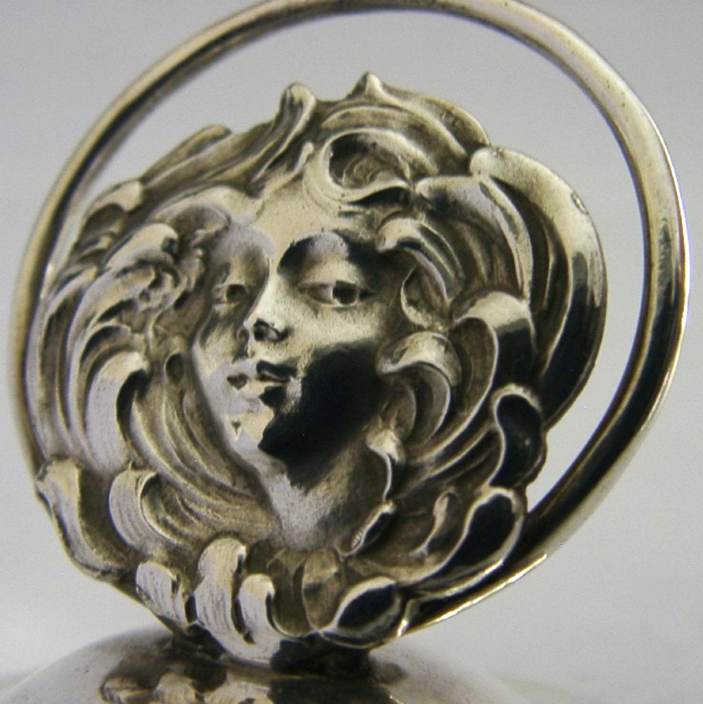 An Art Nouveau sterling silver menu holder featuring a relief face of a maiden with flowing hair set on a domed circular base with British hallmarks. View II