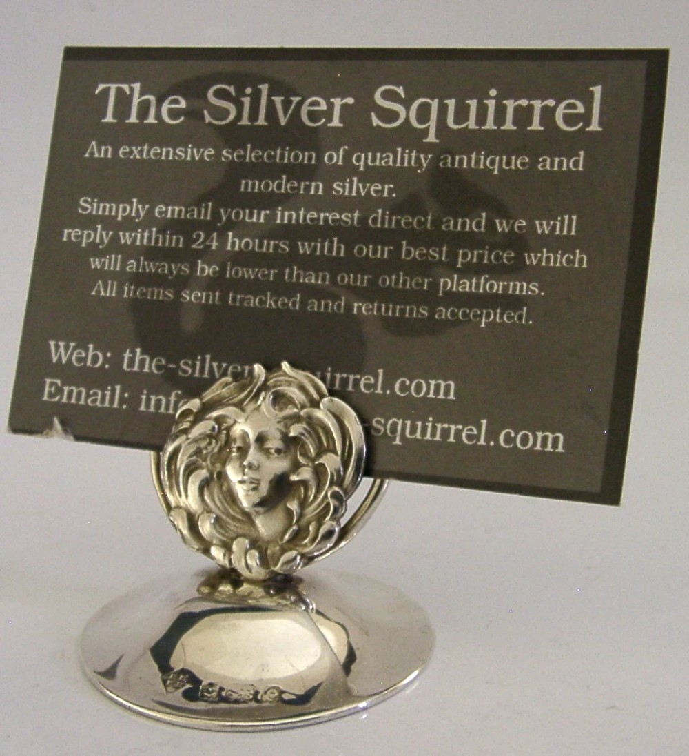 An Art Nouveau sterling silver menu holder featuring a relief face of a maiden with flowing hair set on a domed circular base with British hallmarks. View VI