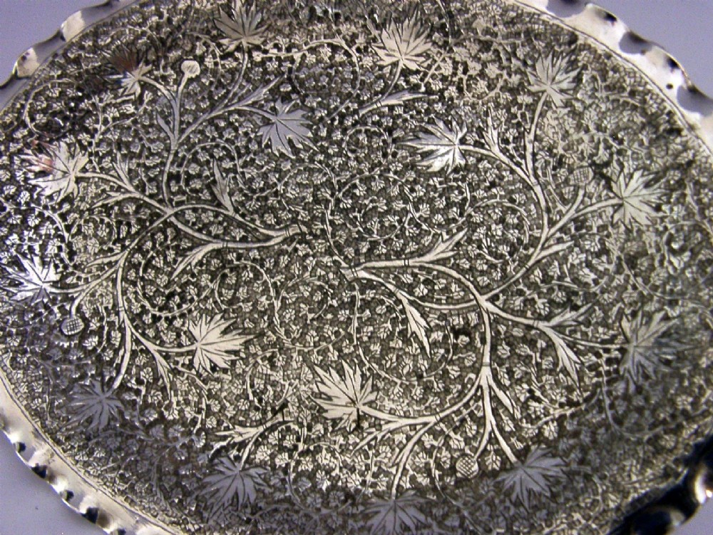 An oval solid silver dish featuring dense chased leaf patterns and a scalloped fluted border. View II