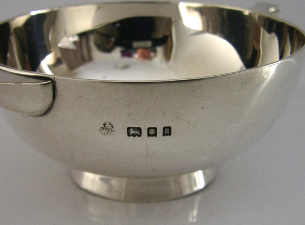 A polished sterling silver shallow drinking cup featuring two flat side handles and British hallmarks stamped on the exterior wall. View II