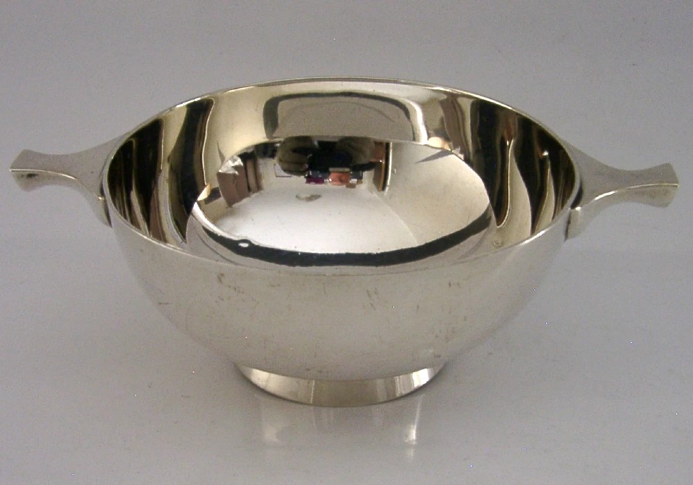 A polished sterling silver shallow drinking cup featuring two flat side handles and British hallmarks stamped on the exterior wall. View III