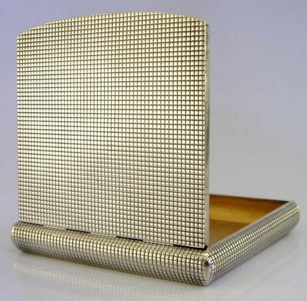An open sterling silver case displaying an engine-turned grid pattern on the exterior and a gilt metallic interior.