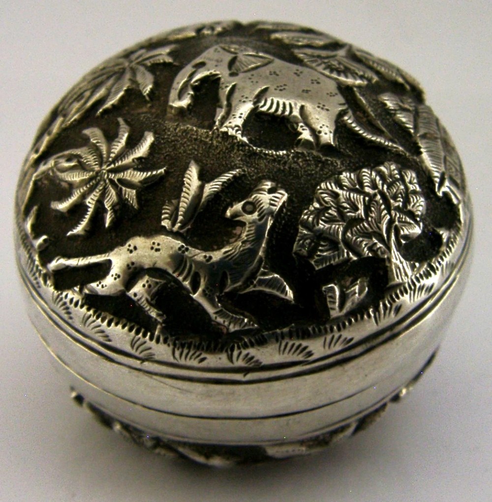 A circular solid silver box with relief repousse carvings depicting an elephant and palm trees in a jungle landscape. View III