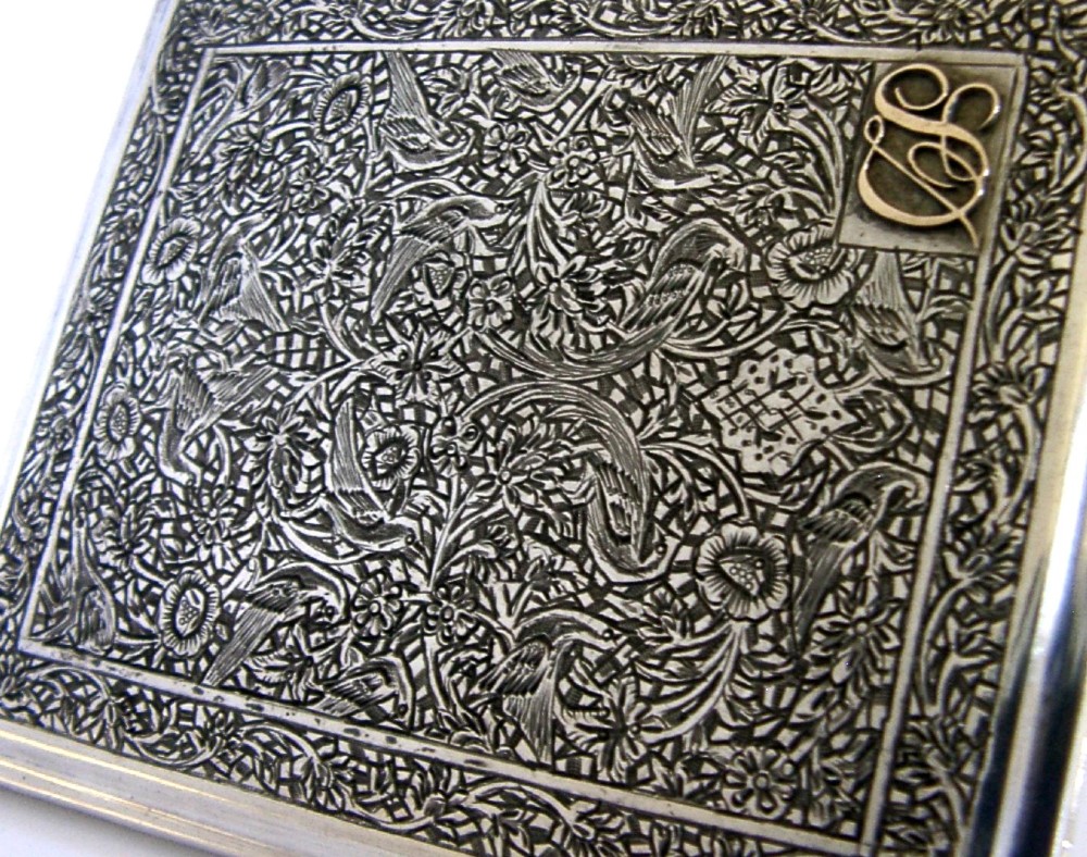 A rectangular solid silver cigarette case featuring dense hand-engraved bird and foliate patterns with a gold monogram in the upper corner. View III