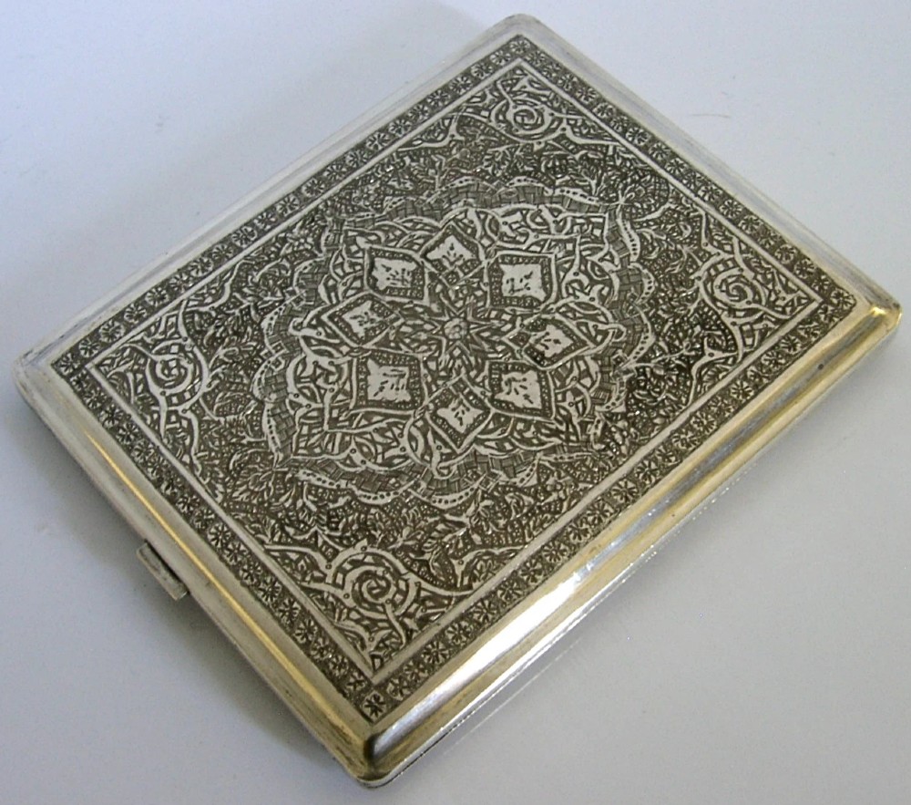 A rectangular solid silver cigarette case featuring dense hand-engraved bird and foliate patterns with a gold monogram in the upper corner. View VI
