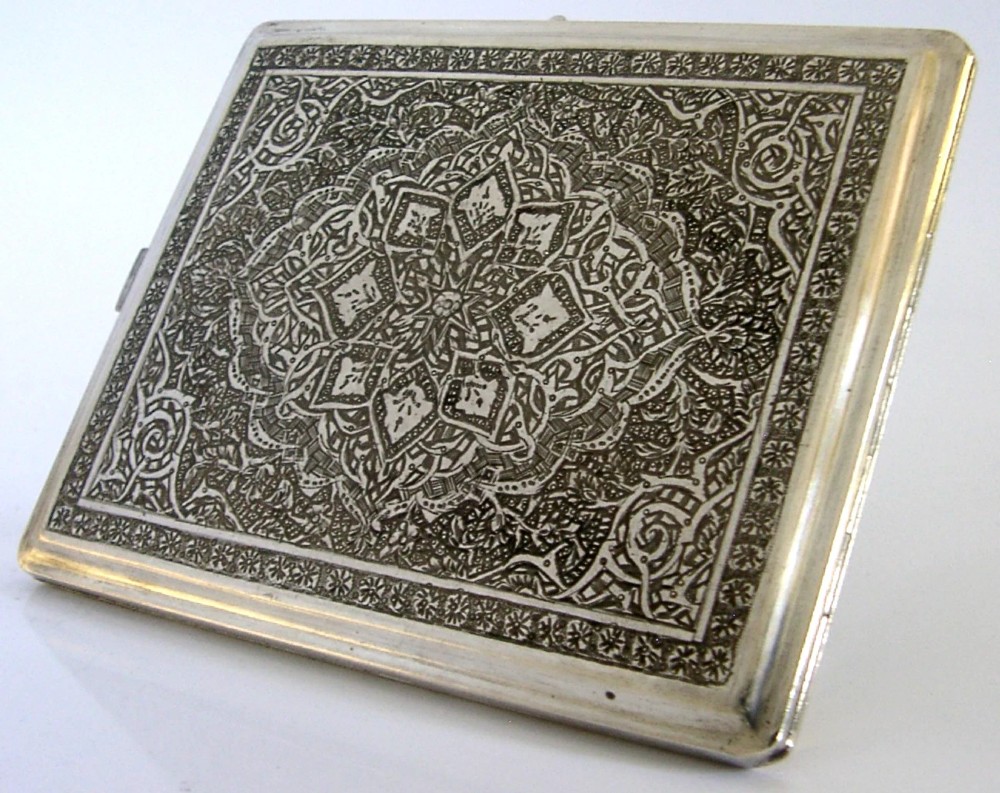 A rectangular solid silver cigarette case featuring dense hand-engraved bird and foliate patterns with a gold monogram in the upper corner. View VII