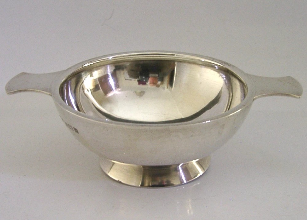 A polished solid sterling silver shallow whisky quaich cup with two flat side lugs resting on a circular raised foot.