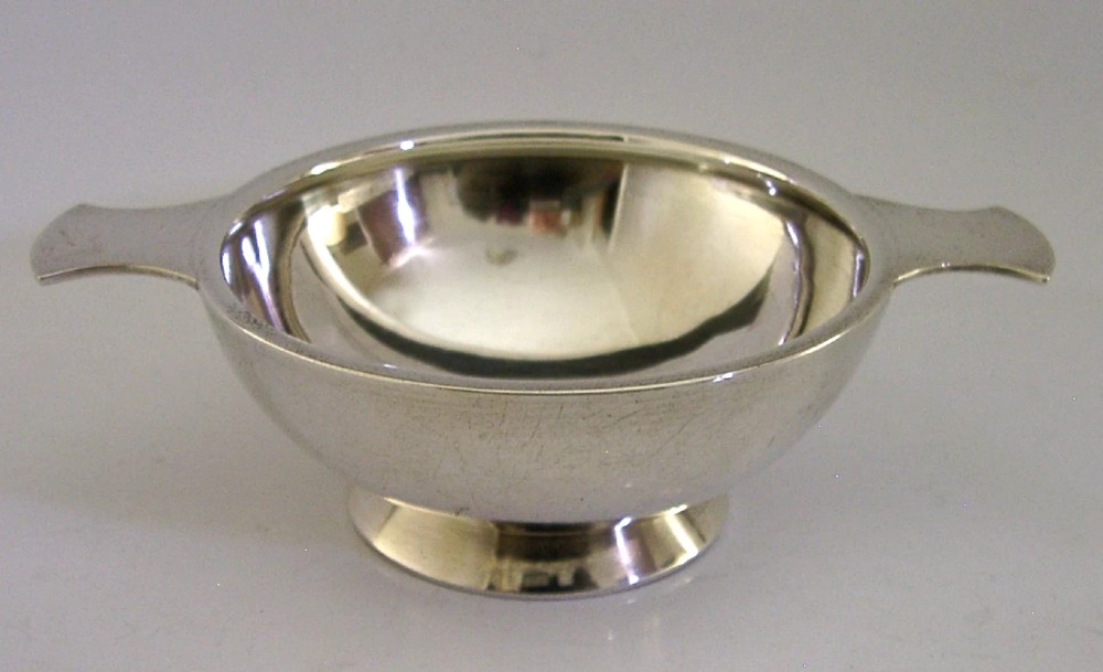 A polished solid sterling silver shallow whisky quaich cup with two flat side lugs resting on a circular raised foot. View III
