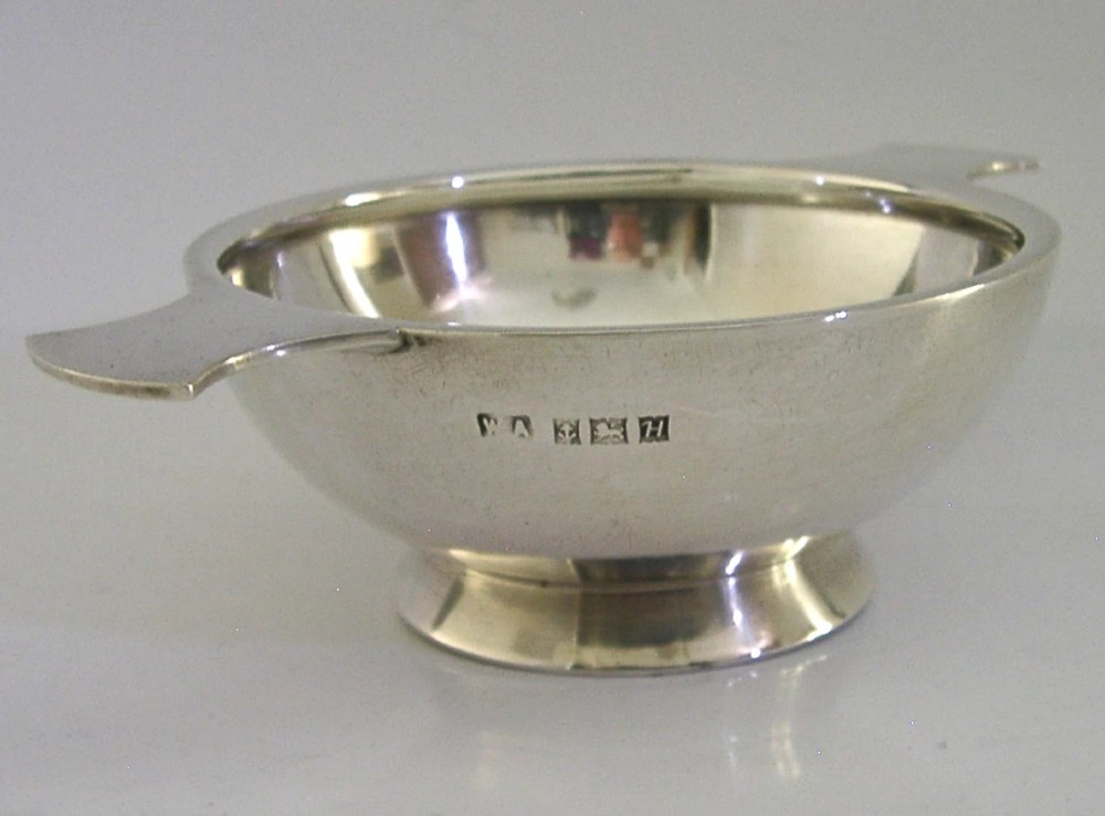 A polished solid sterling silver shallow whisky quaich cup with two flat side lugs resting on a circular raised foot. View IV