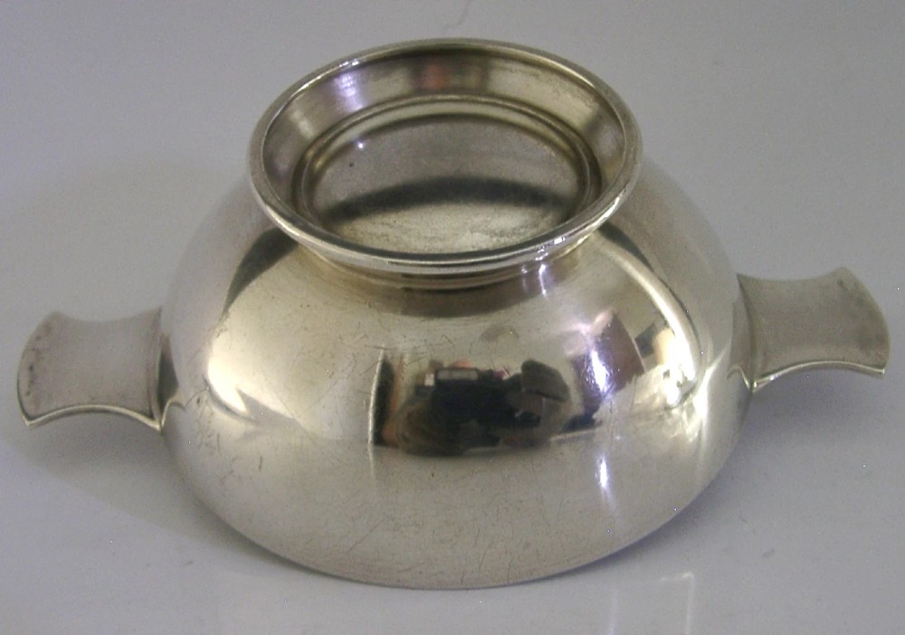 A polished solid sterling silver shallow whisky quaich cup with two flat side lugs resting on a circular raised foot. View V