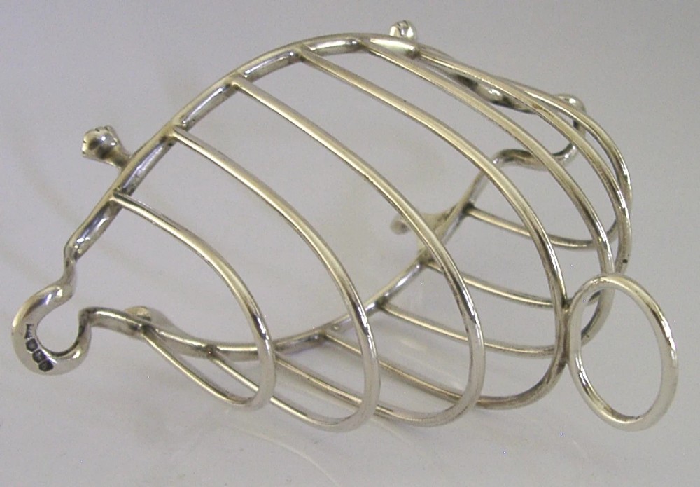 A 1925 English sterling silver six-slice toast rack featuring arched wire dividers, a top ring handle, and small paw feet. View VI