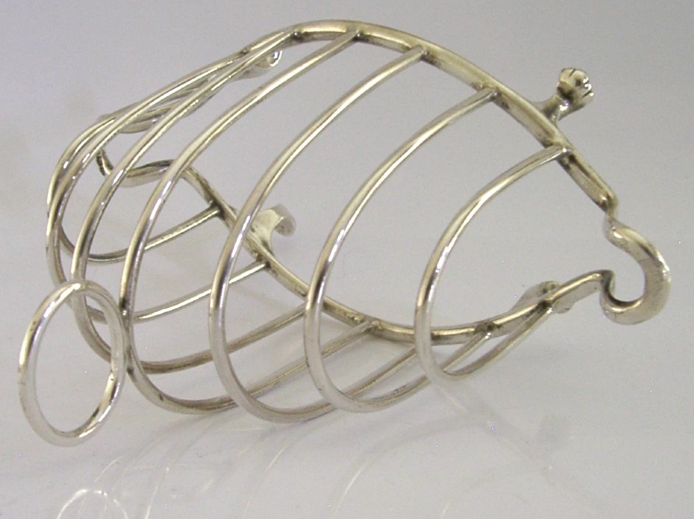 A 1925 English sterling silver six-slice toast rack featuring arched wire dividers, a top ring handle, and small paw feet. View VII