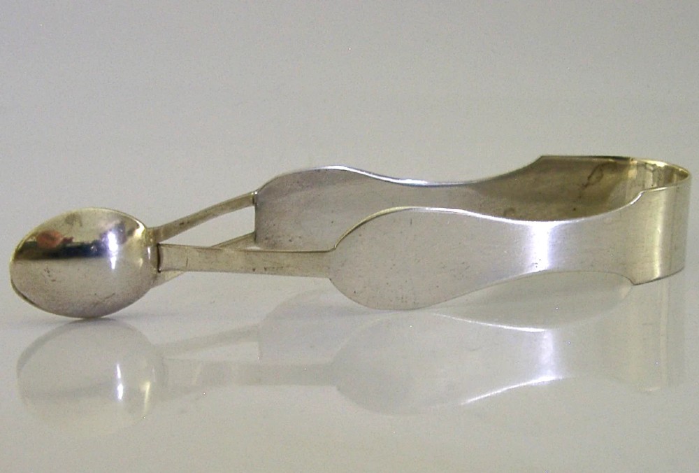 A pair of Edwardian sterling silver sugar tongs featuring smooth contoured arms and spoon-shaped grips.