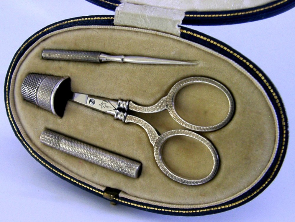 An opened oval fitted leather case displaying an Edwardian sterling silver sewing kit with scissors, thimble, bodkin, and needle case. View II
