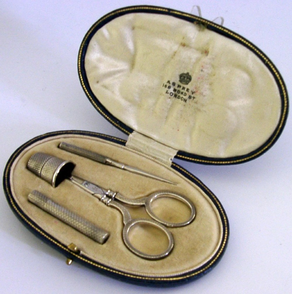 An opened oval fitted leather case displaying an Edwardian sterling silver sewing kit with scissors, thimble, bodkin, and needle case. View III