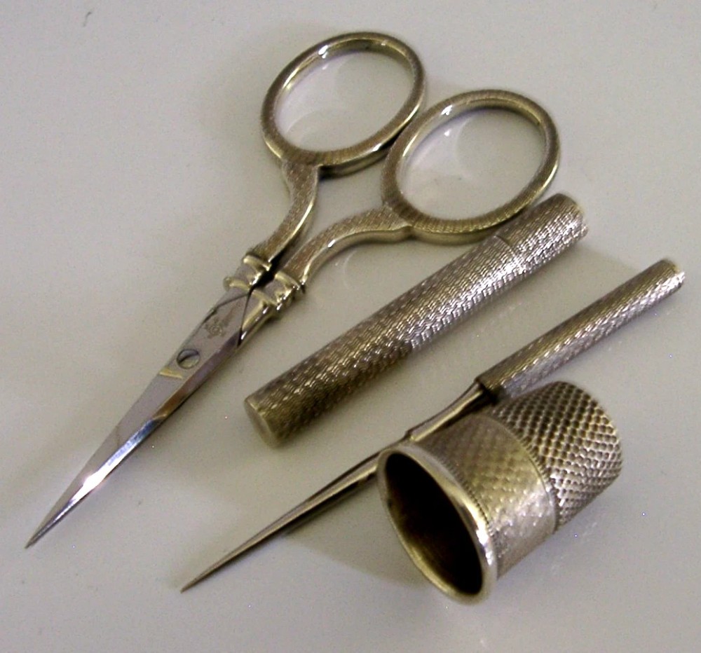 An opened oval fitted leather case displaying an Edwardian sterling silver sewing kit with scissors, thimble, bodkin, and needle case. View IV