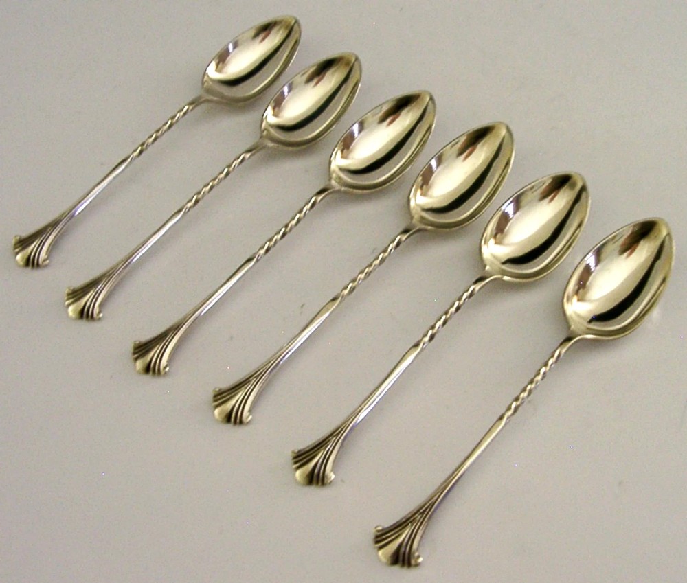 A set of six sterling silver teaspoons featuring twisted stems and shell motif terminals displayed on a light surface.