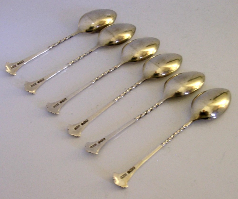 A set of six sterling silver teaspoons featuring twisted stems and shell motif terminals displayed on a light surface. View V
