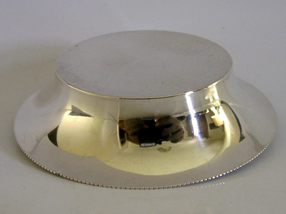 A circular sterling silver dish featuring the embossed coat of arms of the Worshipful Company of Fruiterers in the centre with hallmarks near the rim. View V