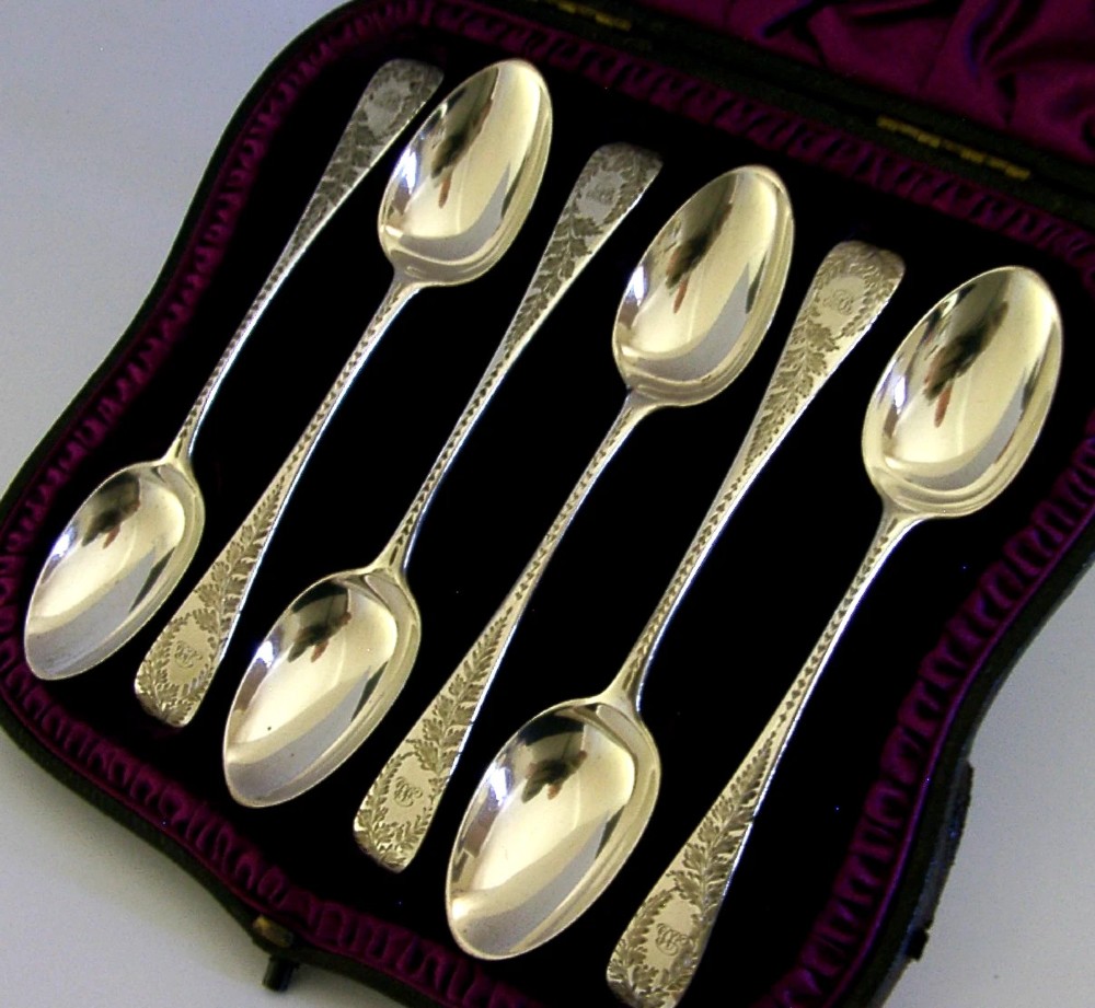 A set of six engraved Victorian sterling silver spoons arranged inside a black fitted presentation case lined with deep purple velvet. View II