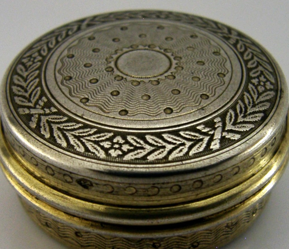 A circular French sterling silver gilt trinket box featuring engine-turned guilloche detailing and a decorative laurel leaf border. View II