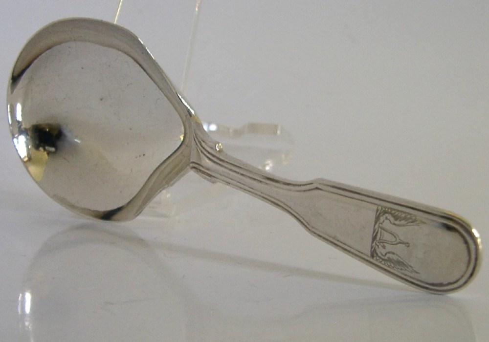 A Victorian sterling silver tea caddy spoon featuring a broad shovel-shaped bowl and an engraved crest on the handle.