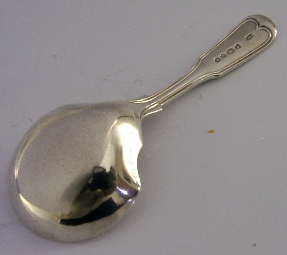 A Victorian sterling silver tea caddy spoon featuring a broad shovel-shaped bowl and an engraved crest on the handle. View IV