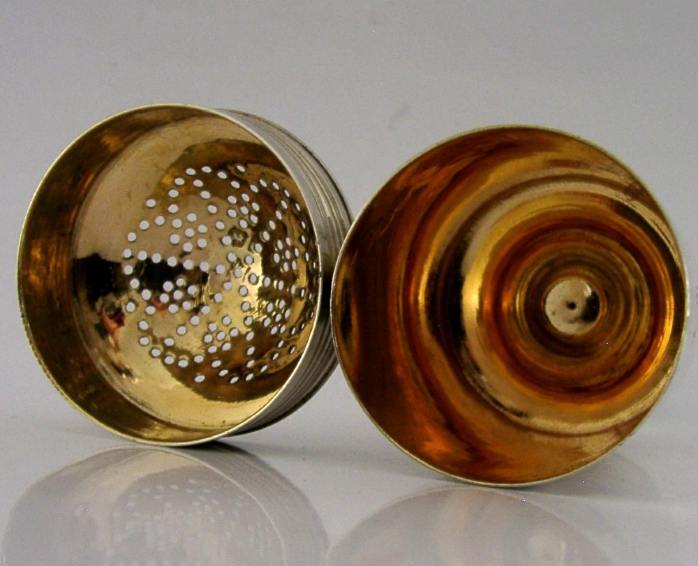 A Georgian sterling silver cylindrical caster top showing a hand-pierced dome with a gilded interior.