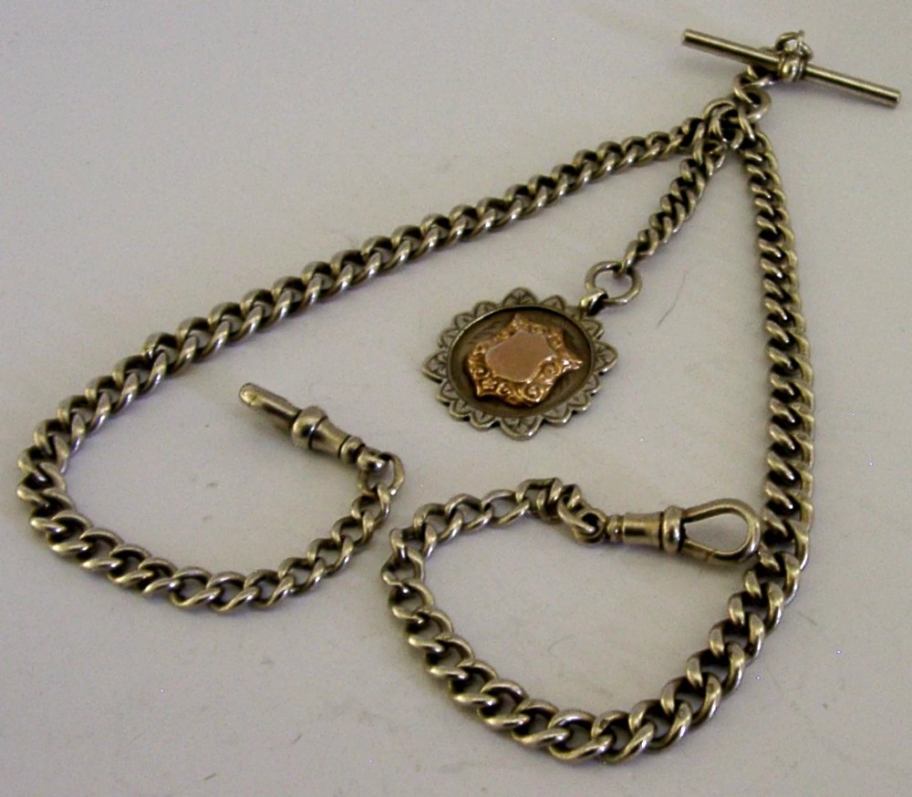 A solid sterling silver double Albert watch chain featuring curb links, a T-bar, two swivel clasps, and a decorative shield fob.