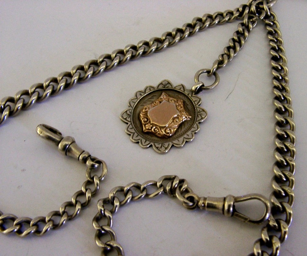 A solid sterling silver double Albert watch chain featuring curb links, a T-bar, two swivel clasps, and a decorative shield fob. View II