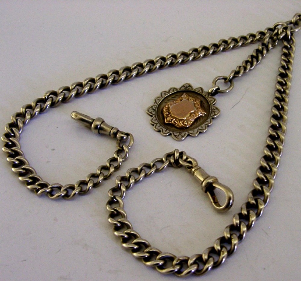 A solid sterling silver double Albert watch chain featuring curb links, a T-bar, two swivel clasps, and a decorative shield fob. View VI