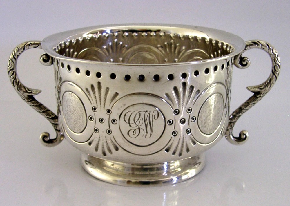An Edwardian sterling silver twin-handled porringer cup with chased oval panels, an engraved monogram, and ornate scroll handles.