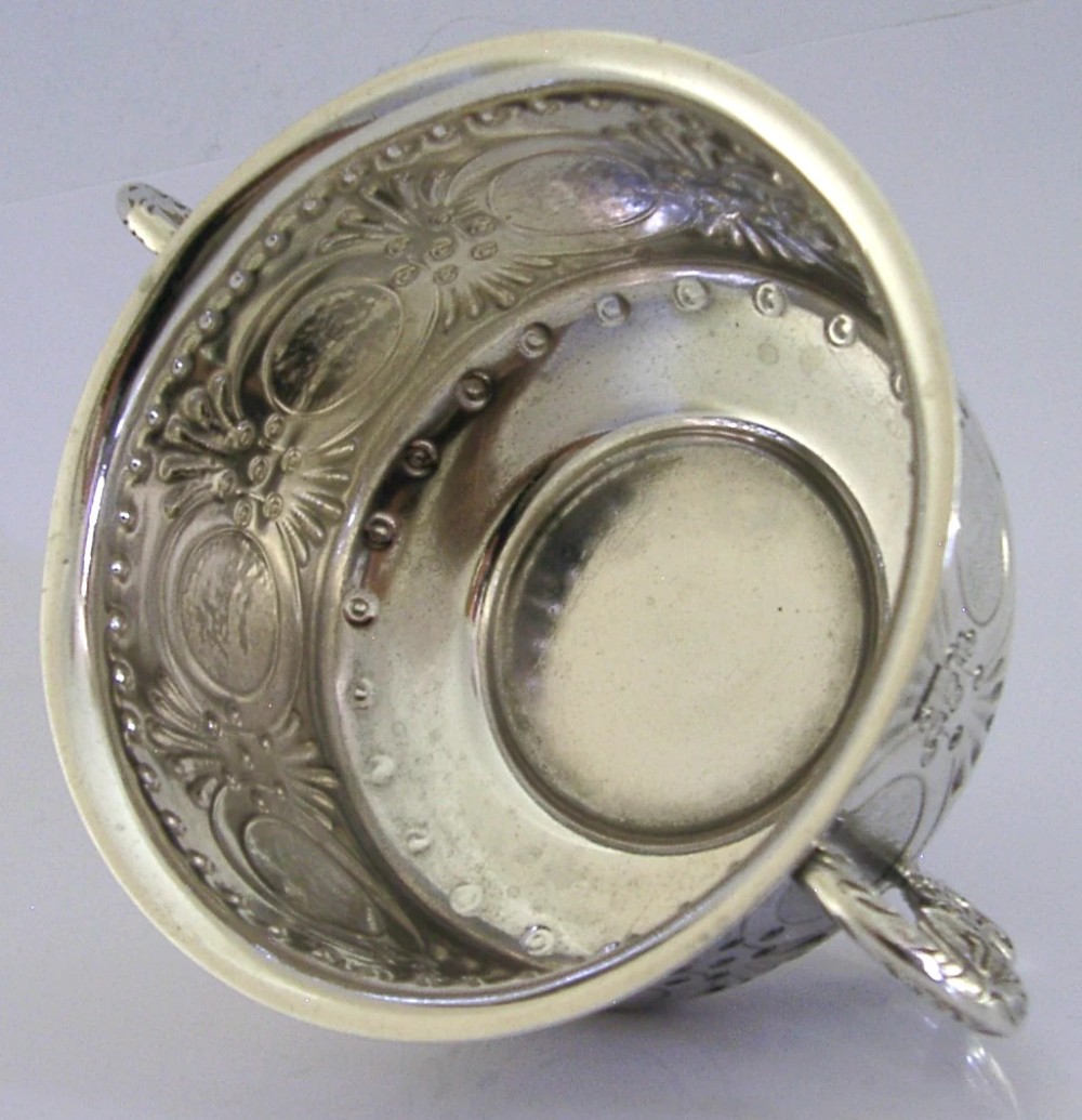 An Edwardian sterling silver twin-handled porringer cup with chased oval panels, an engraved monogram, and ornate scroll handles. View IV