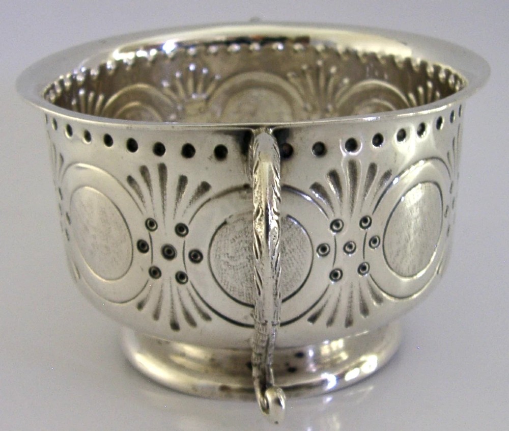 An Edwardian sterling silver twin-handled porringer cup with chased oval panels, an engraved monogram, and ornate scroll handles. View VI