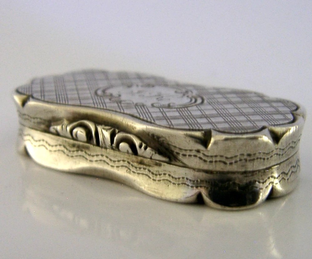 An antique Victorian sterling silver vinaigrette box featuring a shaped lobed outline, engine-turned geometric engraving, and a central engraved monogram cartouche. View VI