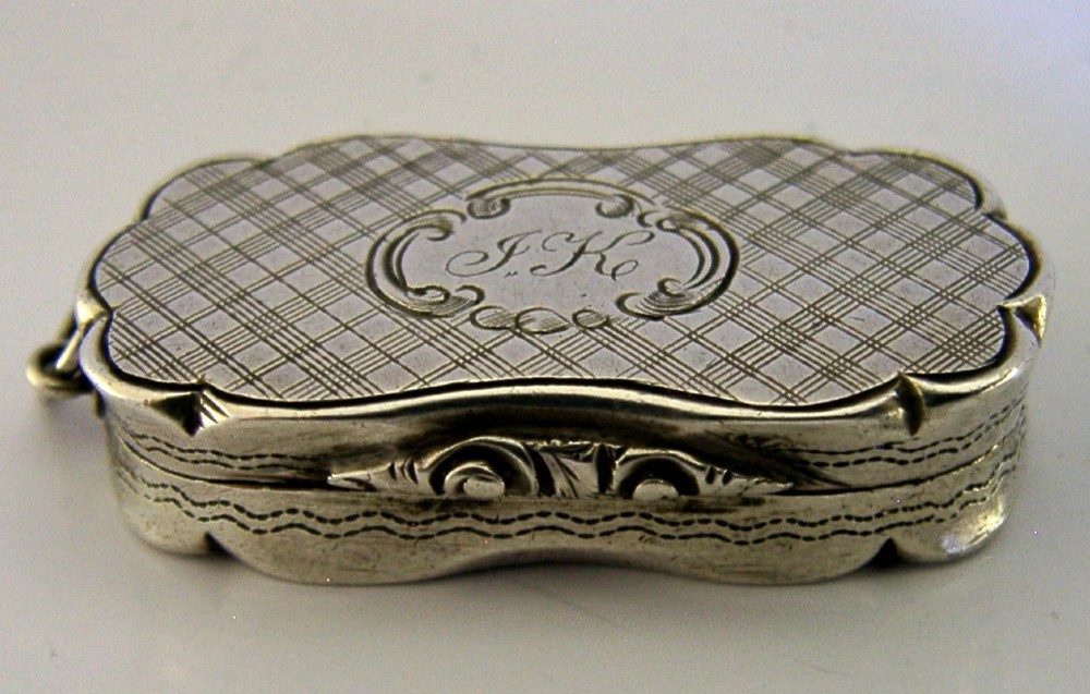 An antique Victorian sterling silver vinaigrette box featuring a shaped lobed outline, engine-turned geometric engraving, and a central engraved monogram cartouche. View VII